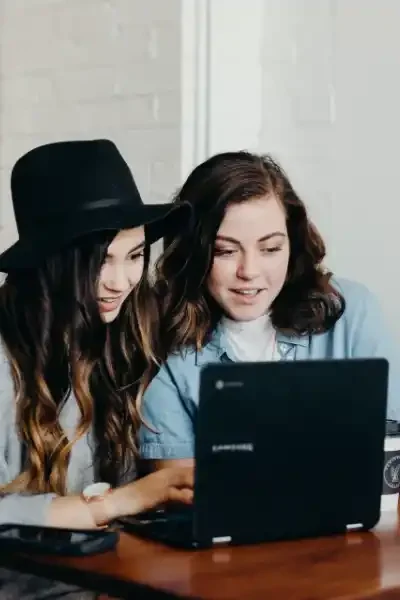 Două femei colaborând la un laptop, stil casual.